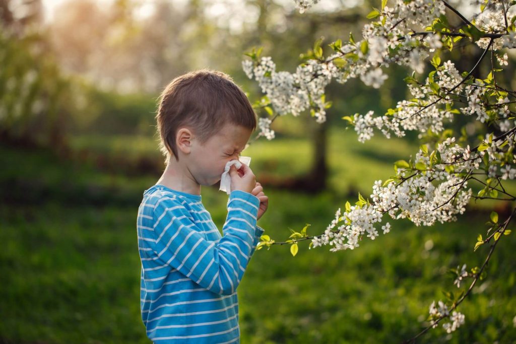 Child suffering allergies and sneezing from pollen. In a park.