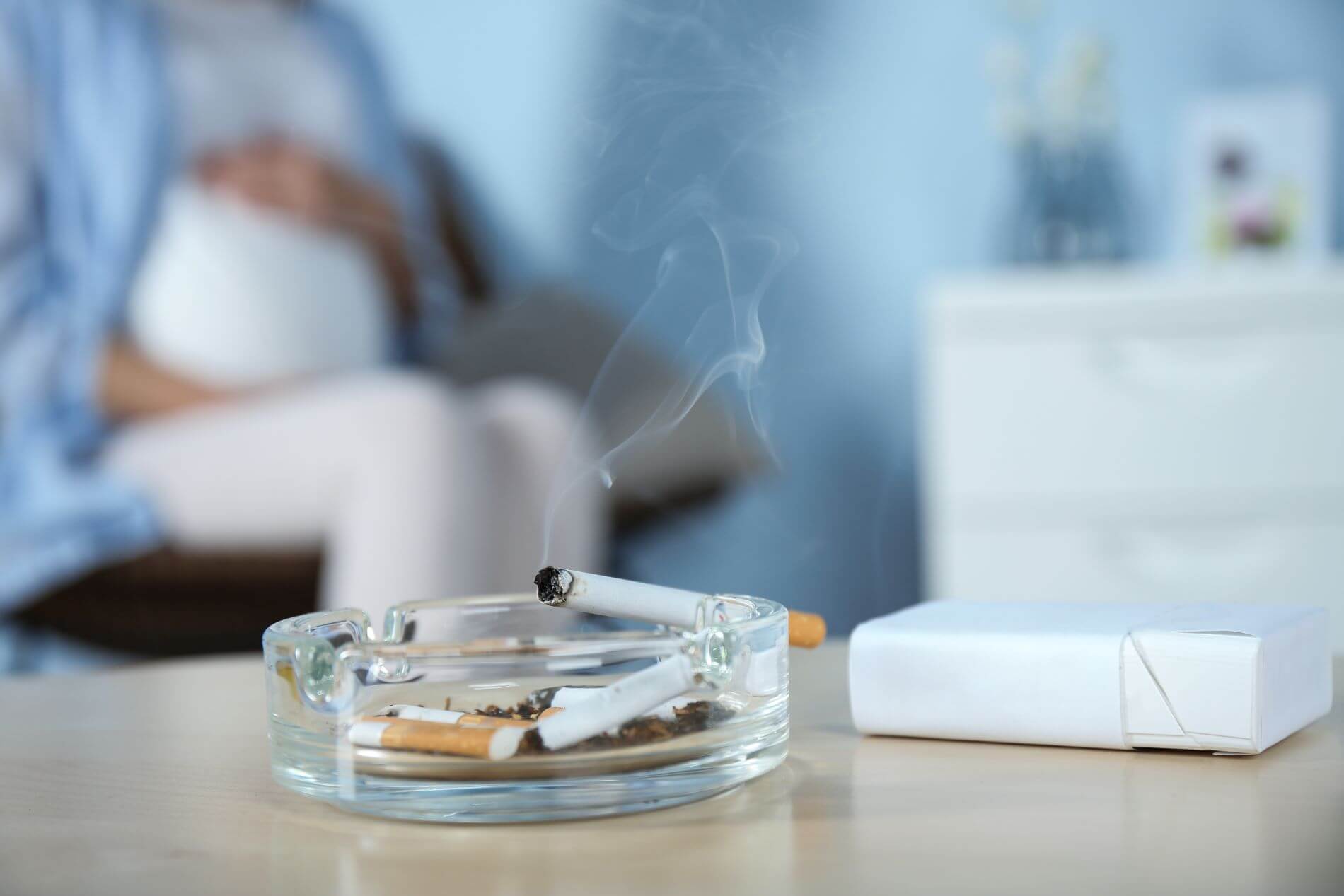 Pregnant woman sitting next to lit cigarettes.