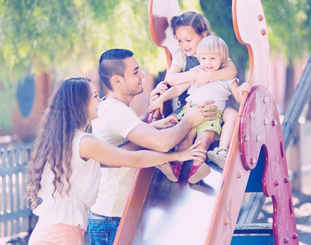 Two children playing on slide with parents.