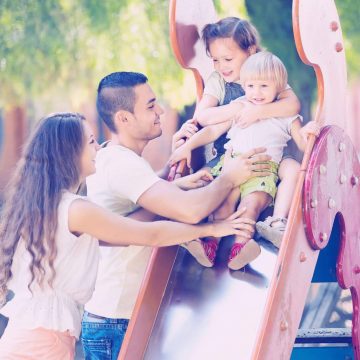Two children playing on slide with parents.