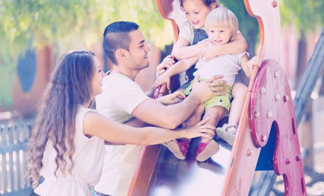 Two children playing on slide with parents.