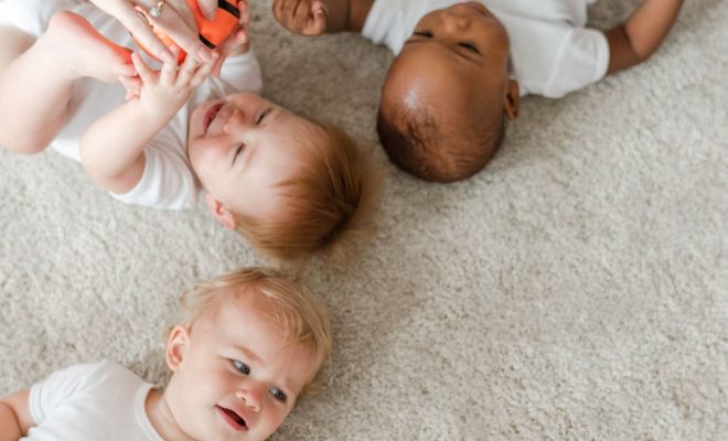 Three babies playing on a rug.