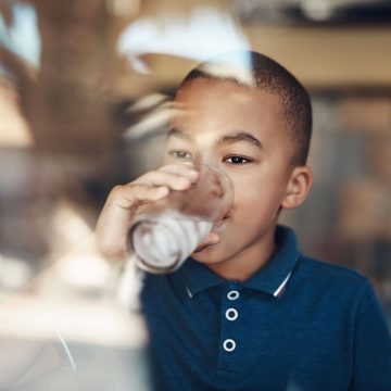 Child drinking cup of water by a window.