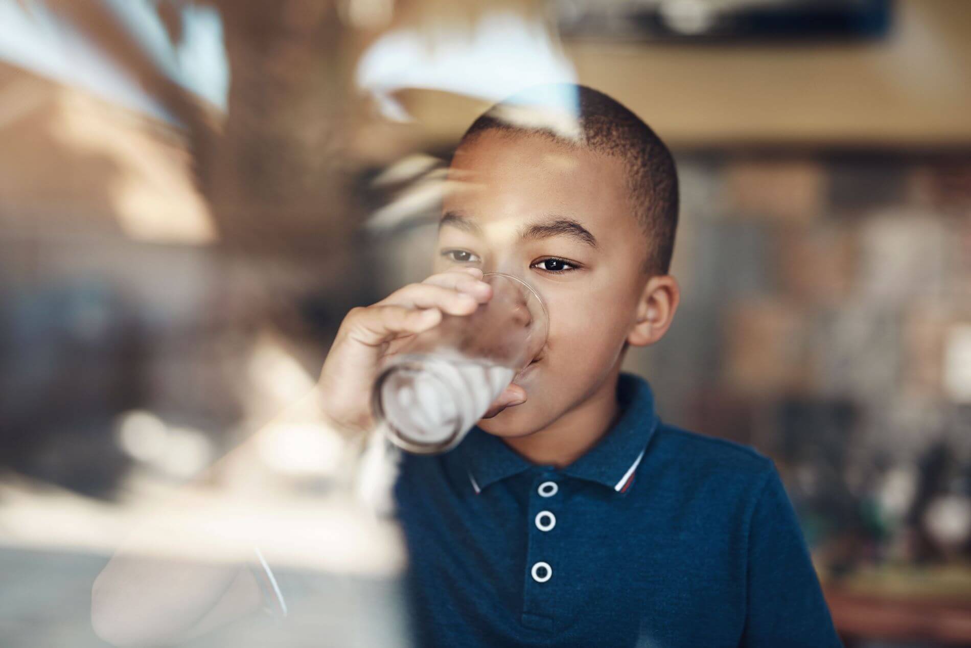 Child drinking cup of water by a window.