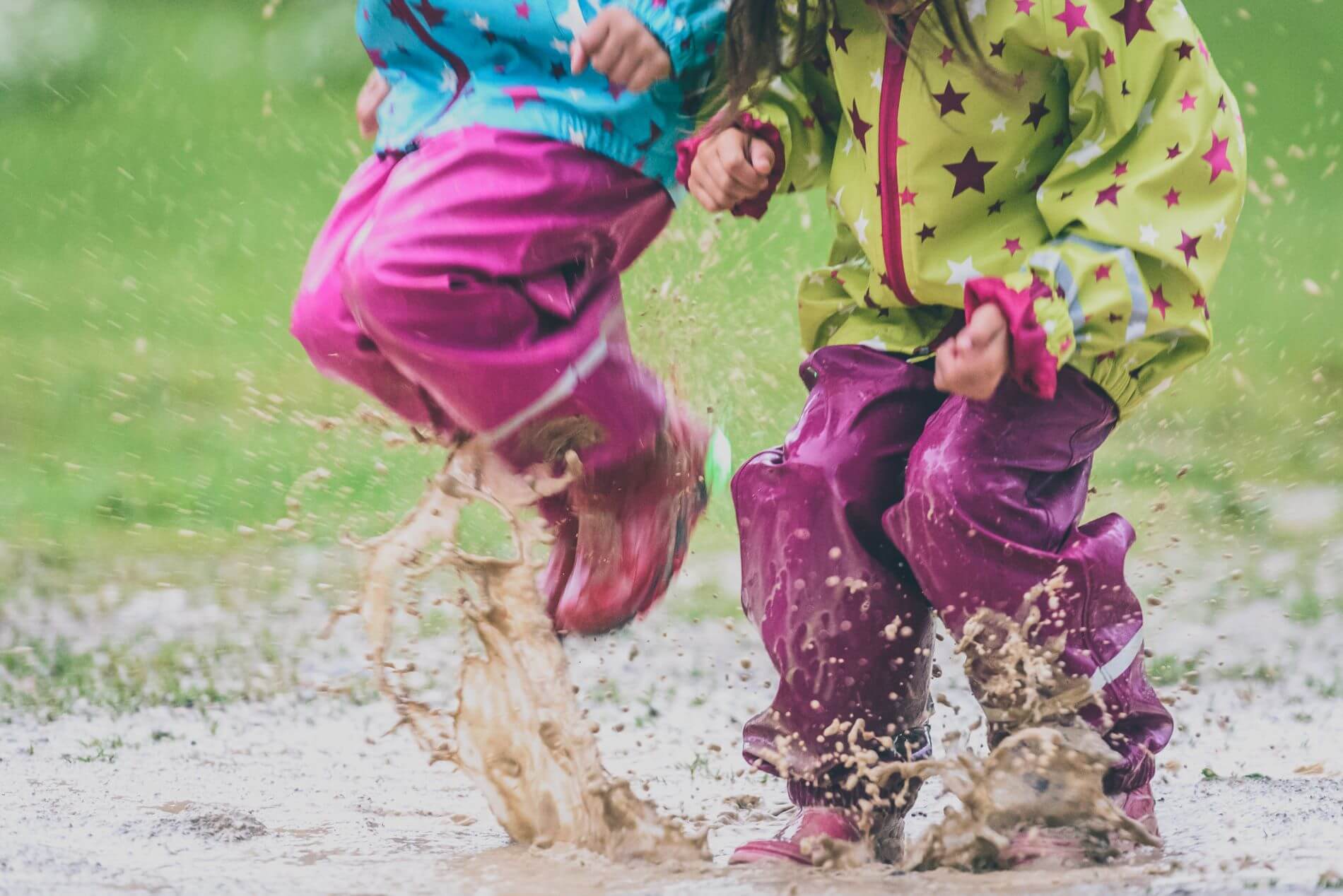 Two kids playing in a puddle with rain coats and waterproof pants.