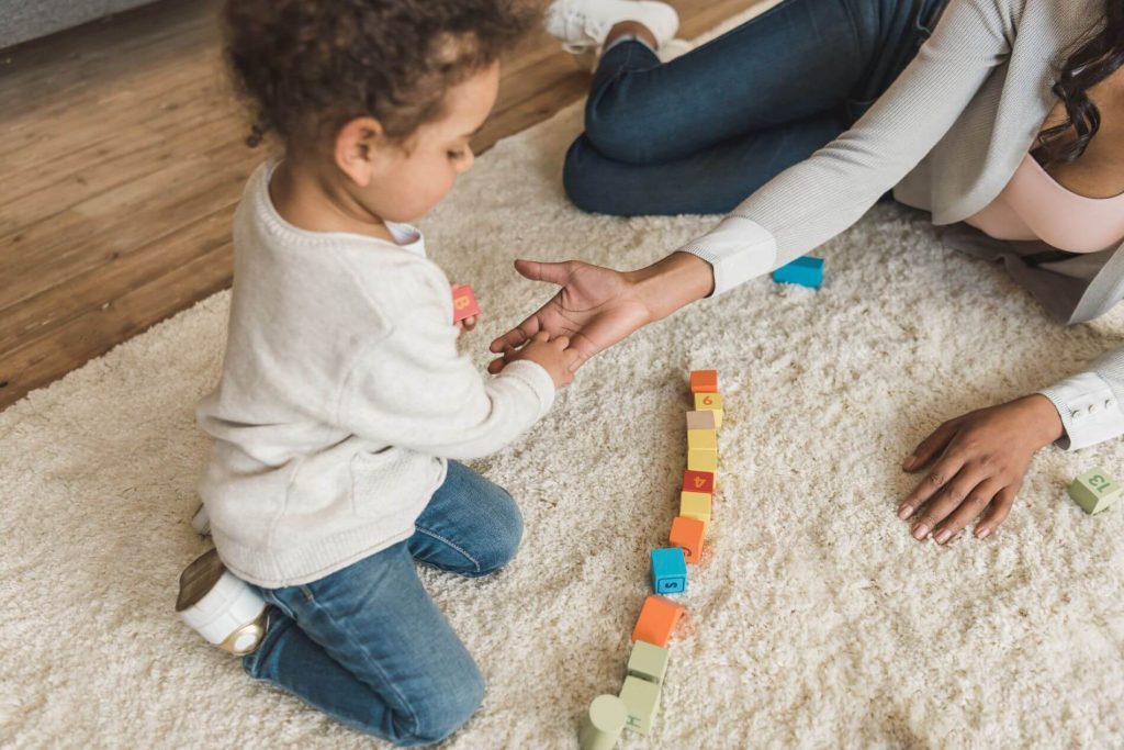 Child playing blocks with woman on carpet in bedroom.