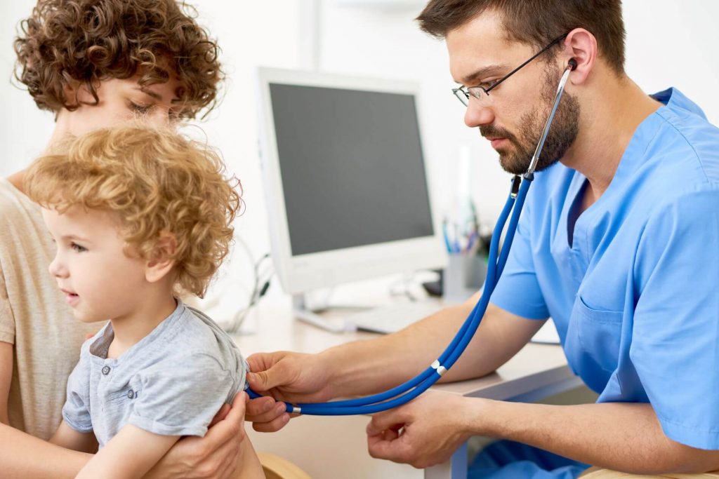 Doctor using stethoscope while mother holds child.