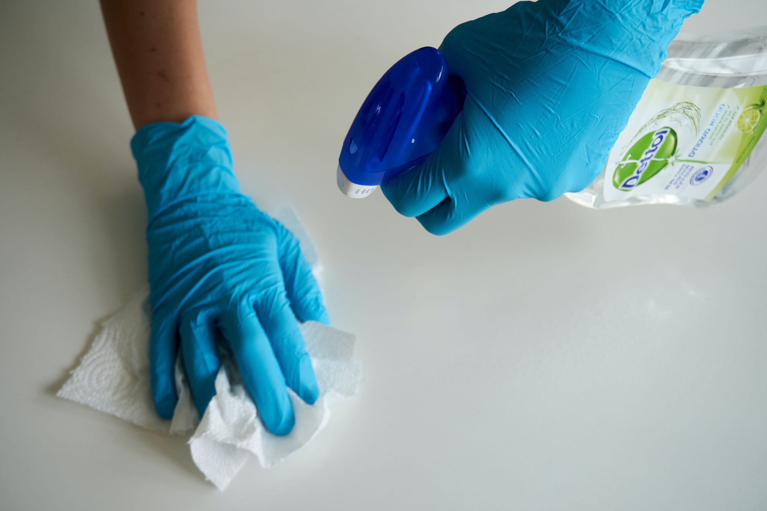 Hands covered with gloves cleaning a counter with spray and paper towel.
