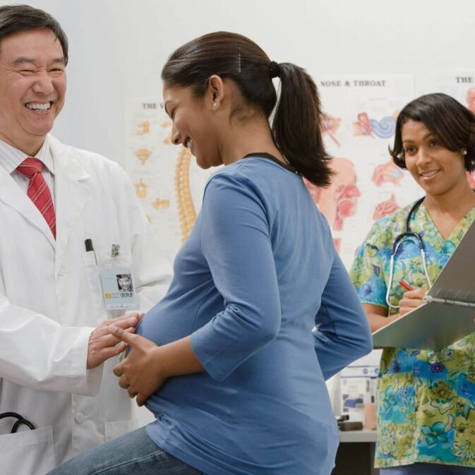 Pregnant woman meeting with doctor and nurse in office.
