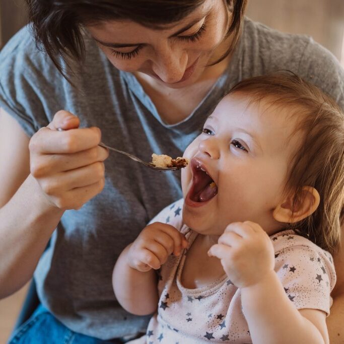 Mother feeding with spoon her little baby at home.