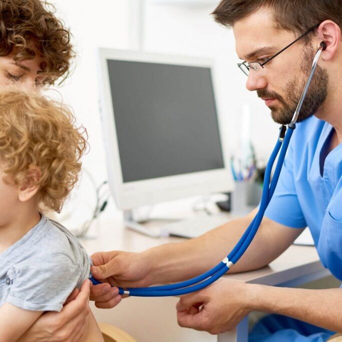 Doctor using stethoscope while mother holds child.