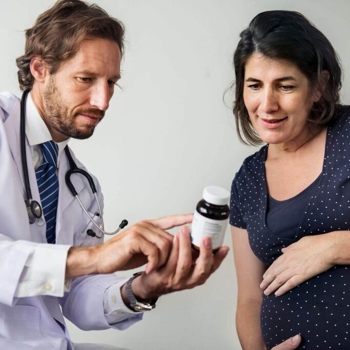 Pregnant woman talking with doctor while looking at medicine ingredients.