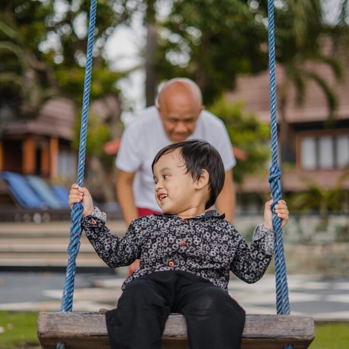 Child on swing being pushed on the swing by grandfather.