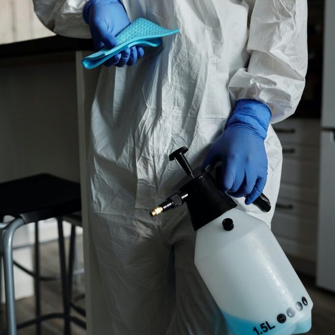 Person with protective gear with industrial cleaning spay and cloth.
